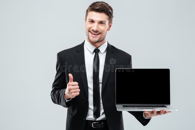 Homme d'affaires gai tenant l'ordinateur portable d'écran vide et montrant des pouces images stock Homme d'affaires gai tenant l'ordinateur portable d'écran vide et montrant des pouces images stock