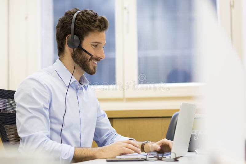 Homme d'affaires heureux dans le bureau au téléphone, casque, Skype image stock Homme d'affaires heureux dans le bureau au téléphone, casque, Skype image stock