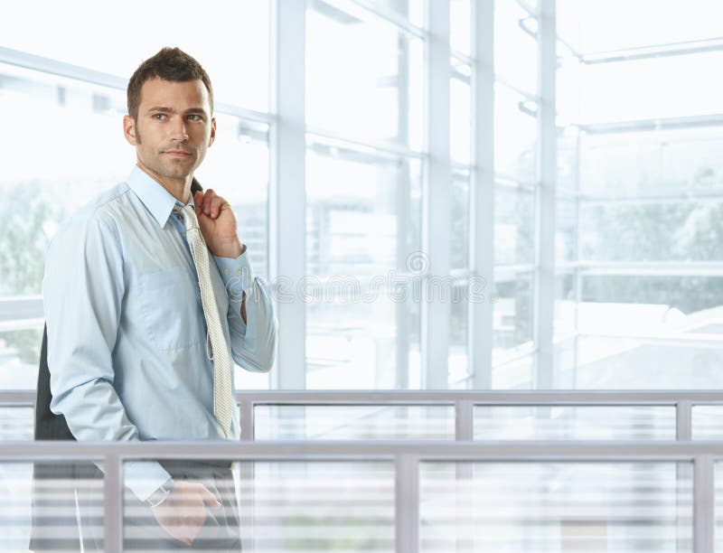 Casual businessman standing in front of glass walls in office lobby, smiling. Casual businessman standing in front of glass walls in office lobby, smiling.