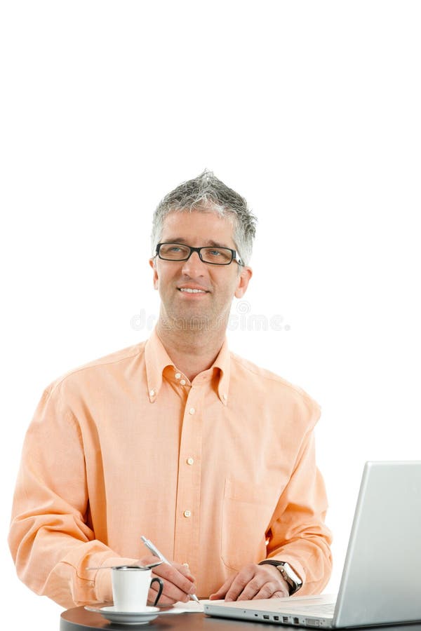Casual businessman wearing orange shirt and jeans, standing at coffee table, using laptop computer, writing notes. Isolated on white. Casual businessman wearing orange shirt and jeans, standing at coffee table, using laptop computer, writing notes. Isolated on white.