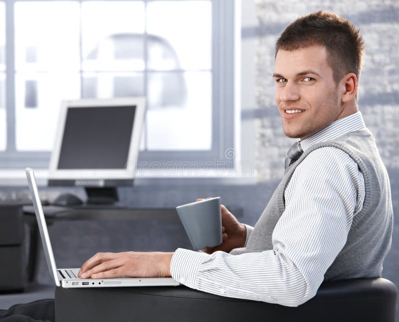 Casual businessman sitting in armchair, drinking tea, working on laptop, smiling. Casual businessman sitting in armchair, drinking tea, working on laptop, smiling.