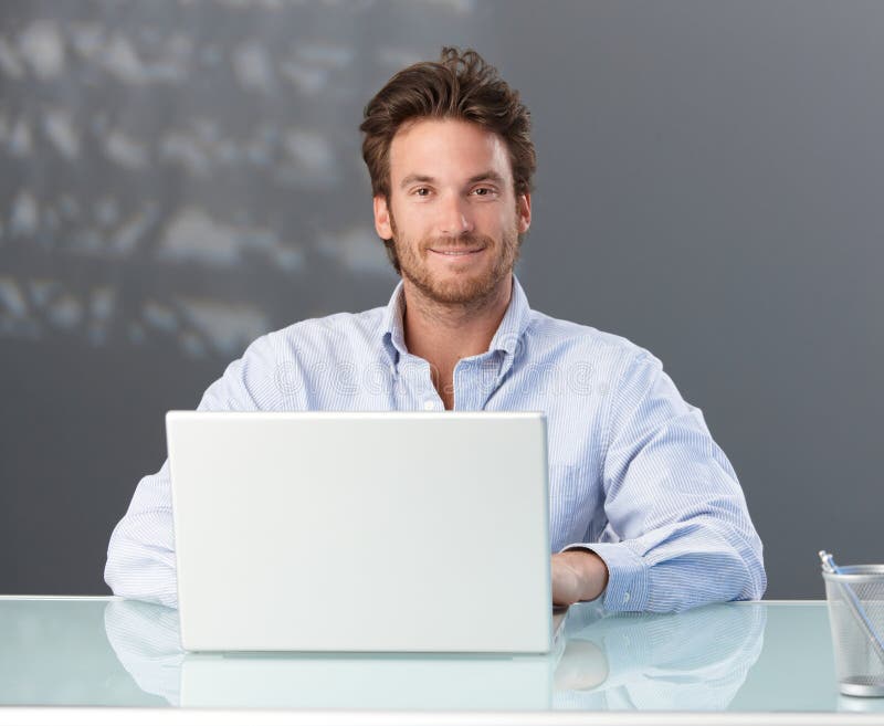 Casual businessman sitting in office with laptop computer, smiling at camera. Casual businessman sitting in office with laptop computer, smiling at camera.