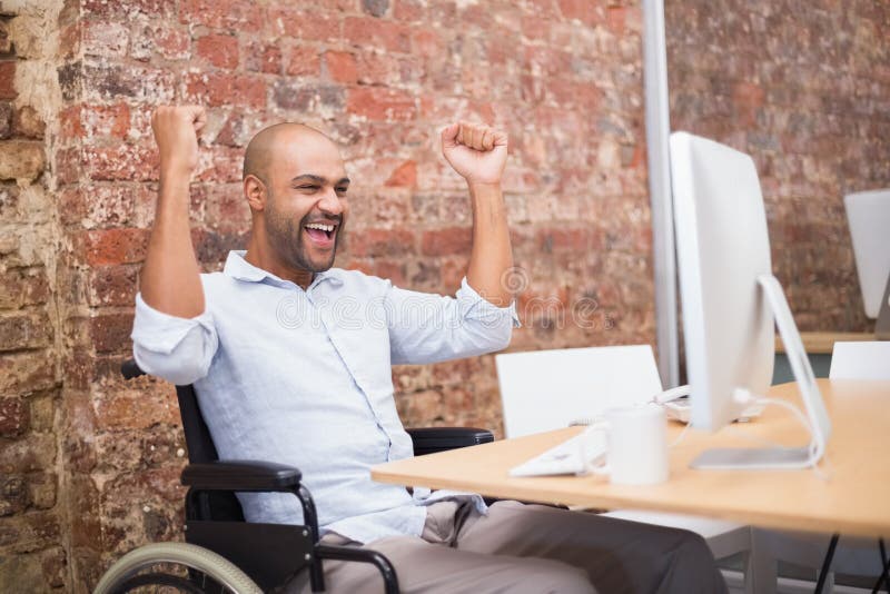 Casual businessman in wheelchair cheering at his desk in the office. Casual businessman in wheelchair cheering at his desk in the office