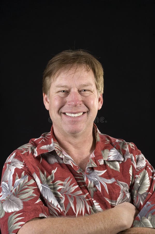 Happy smiling casual businessman in a floral Hawaiin style shirt over a black background. Happy smiling casual businessman in a floral Hawaiin style shirt over a black background