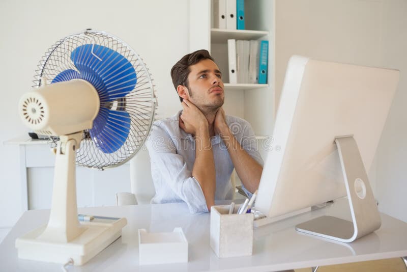 Casual businessman sitting at desk with electric fan in his office. Casual businessman sitting at desk with electric fan in his office