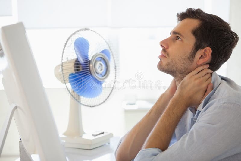 Casual businessman sitting at desk with electric fan in his office. Casual businessman sitting at desk with electric fan in his office