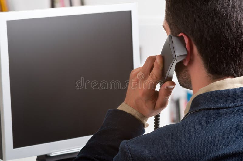 Casual businessman talking over the phone and looking at an empty computer screen. Casual businessman talking over the phone and looking at an empty computer screen