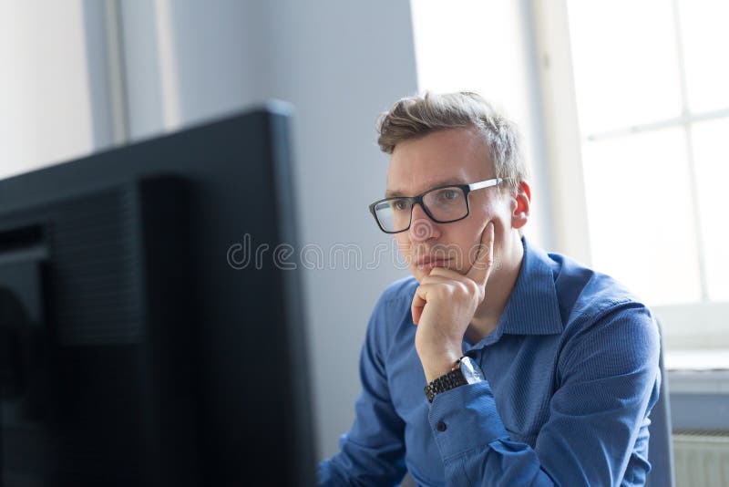 Thoughtful casual businessman wearing eyeglasses, working in office, sitting at desk, typing on keyboard, looking at computer screen. Thoughtful casual businessman wearing eyeglasses, working in office, sitting at desk, typing on keyboard, looking at computer screen.