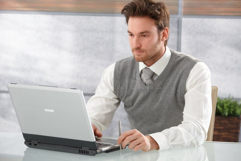 Casual businessman working on laptop in office, looking at screen. Casual businessman working on laptop in office, looking at screen.