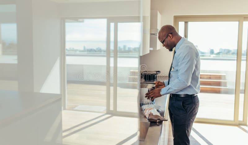 Man dressed in formals preparing breakfast in kitchen. Businessman using oven to prepare breakfast. Man dressed in formals preparing breakfast in kitchen. Businessman using oven to prepare breakfast.