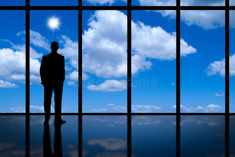 A silhouette of a businessman looking out of a high rise office building window at blue sky, clouds and bright sun. A silhouette of a businessman looking out of a high rise office building window at blue sky, clouds and bright sun.