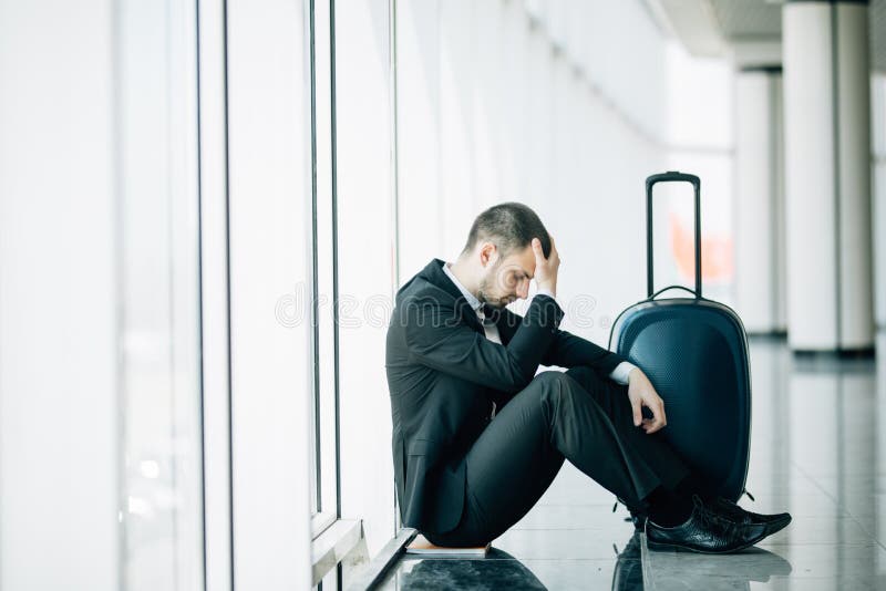 Homme d'affaires s'asseyant à l'aéroport terminal sur le plancher avec le retard de vol de valise, contact de deux mains à la têt photographie stock libre de droits Homme d'affaires s'asseyant à l'aéroport terminal sur le plancher avec le retard de vol de valise, contact de deux mains à la têt photographie stock libre de droits