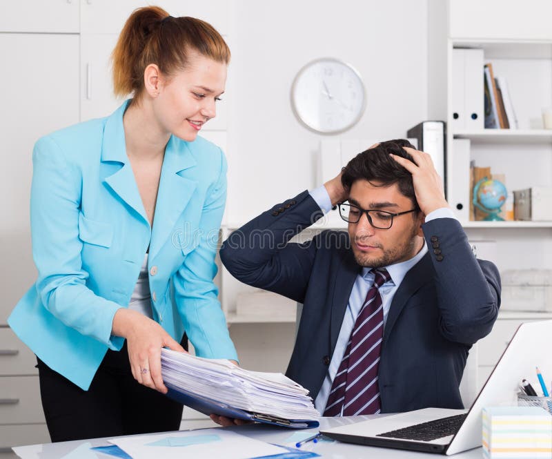 Overworked businessman looking at female colleague bringing new sheaf of papers. Overworked businessman looking at female colleague bringing new sheaf of papers