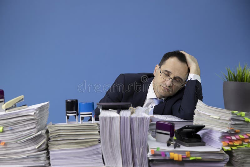 Overwhelmed overworked businessman asleep at office desk loaded of paperwork, lot of papers and documents. business. Overwhelmed overworked businessman asleep at office desk loaded of paperwork, lot of papers and documents. business