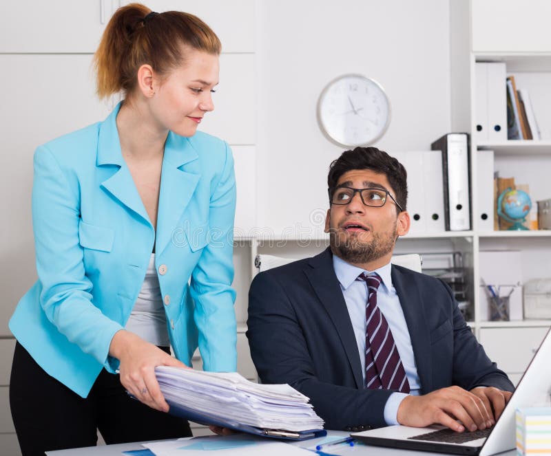 Overworked businessman looking at female colleague bringing new sheaf of papers. Overworked businessman looking at female colleague bringing new sheaf of papers