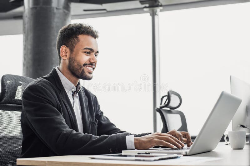 Homme d'affaires travaillant sur l'ordinateur. Jeune homme de sourire à l'aide de l'ordinateur portable au bureau. Concept d'affai images stock