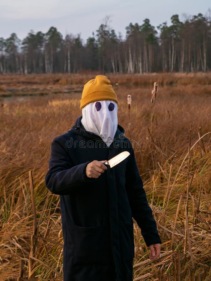 Homme dangereux avec un chiffon blanc sur le visage et un couteau dans la main sur les roseaux le soir. halloween. vue verticale images stock