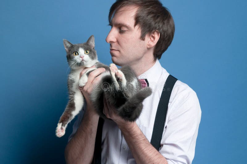 Homme dans la chemise rose et la bretelle noire tenant et regardant le chat gris et blanc mignon image stock Homme dans la chemise rose et la bretelle noire tenant et regardant le chat gris et blanc mignon image stock