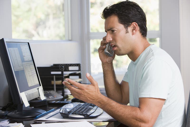 Homme dans le Home Office au téléphone utilisant l'ordinateur photo stock Homme dans le Home Office au téléphone utilisant l'ordinateur photo stock