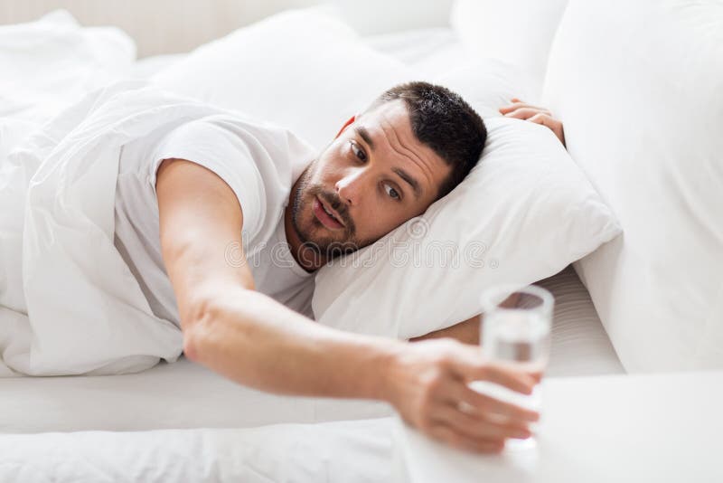 Homme dans le lit et atteinte au verre de l'eau à la maison photos stock Homme dans le lit et atteinte au verre de l'eau à la maison photos stock