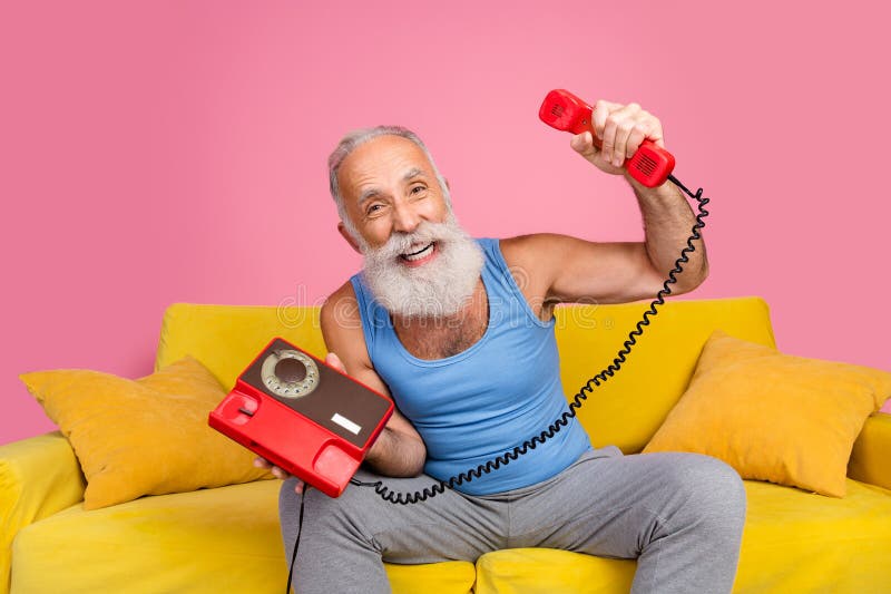 Homme de haut niveau profitant du temps de loisir à la maison avec un téléphone rétro sur un canapé lumineux à l'intérieur images stock