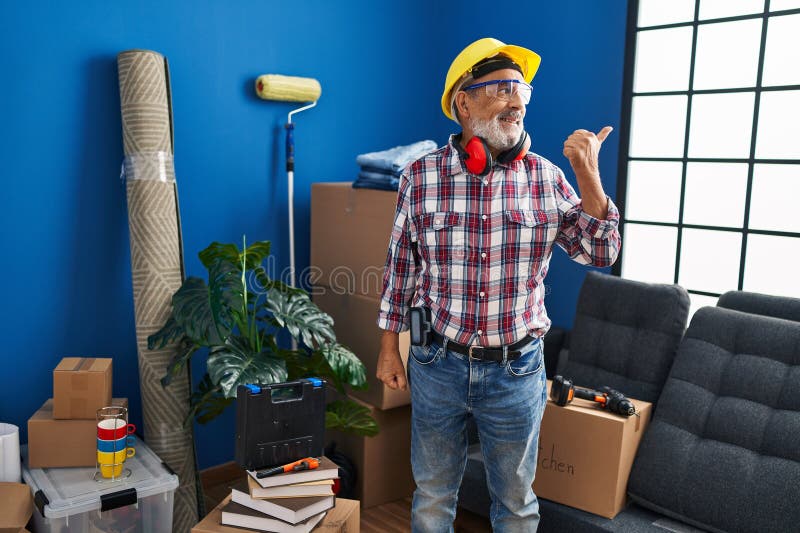 Homme de haut rang joyeux dans casque dur et lunettes de sécurité souriant et en marchant tout en pointant joyeusement vers sa nou photographie stock