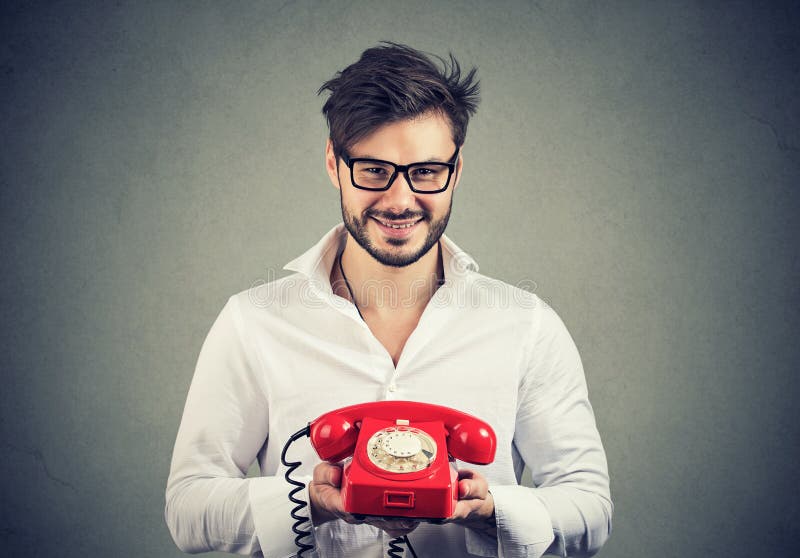 Homme de sourire en chemise blanche et verres tenant le fonctionnement rouge de téléphone pour le service à la clientèle photo libre de droits Homme de sourire en chemise blanche et verres tenant le fonctionnement rouge de téléphone pour le service à la clientèle photo libre de droits