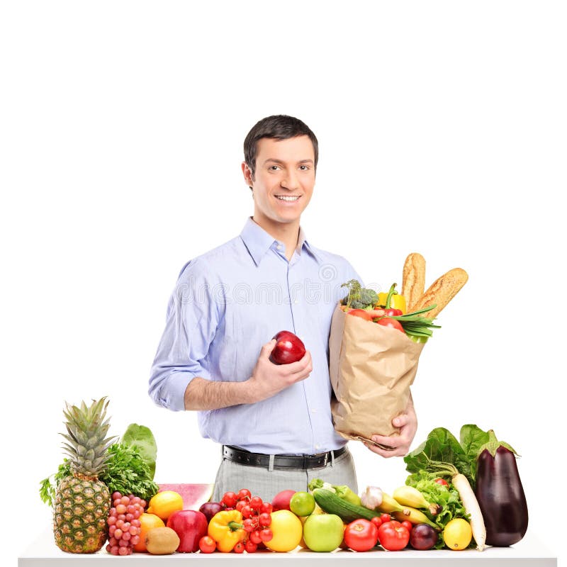 Homme de sourire tenant une pomme et un sac avec des produits alimentaires images libres de droits Homme de sourire tenant une pomme et un sac avec des produits alimentaires images libres de droits