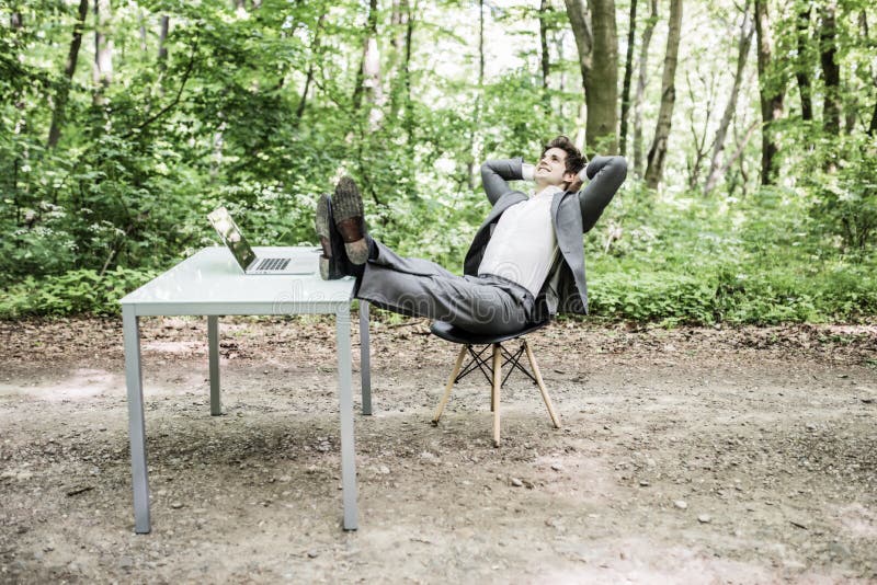 Homme décontracté d'affaires dans le costume avec des têtes frais généraux et jambes sur le bureau après travail réussi en parc v images stock Homme décontracté d'affaires dans le costume avec des têtes frais généraux et jambes sur le bureau après travail réussi en parc v images stock