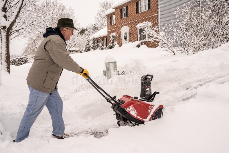 Berks County, Pennsylvania-February 2, 2021:  Senior man using a snow blower to clear his sidewalk and driveway after snowstorm. Berks County, Pennsylvania-February 2, 2021:  Senior man using a snow blower to clear his sidewalk and driveway after snowstorm.