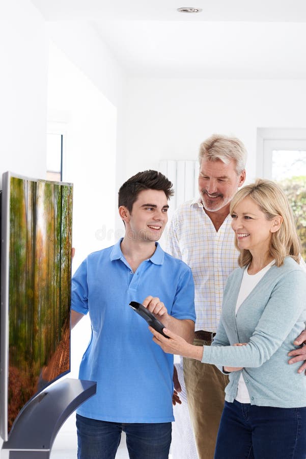 Homme démontrant la nouvelle télévision aux couples mûrs à la maison image stock Homme démontrant la nouvelle télévision aux couples mûrs à la maison image stock