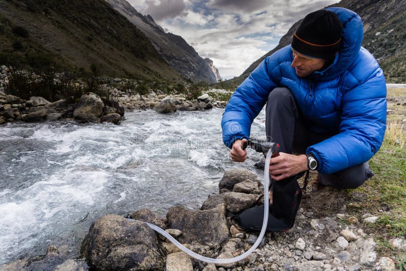 Homme en eau potable de filtrage vers le bas de veste bleue d'une rivière de montagne au Pérou photos stock Homme en eau potable de filtrage vers le bas de veste bleue d'une rivière de montagne au Pérou photos stock