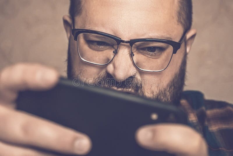 Homme en jeu vidéo mobile de jeu fâché en verre, tenant le smartphone par les deux mains photos libres de droits Homme en jeu vidéo mobile de jeu fâché en verre, tenant le smartphone par les deux mains photos libres de droits
