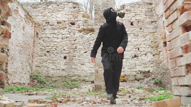 Homme en masque à gaz et vêtements noirs est parmi les ruines bâtiment abandonné. survivant du concept de stalker après la guerre clips vidéos