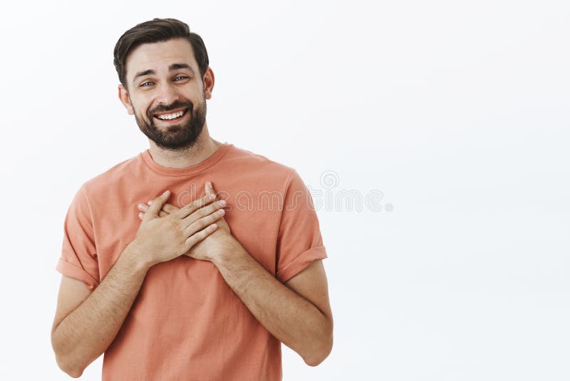 Homme européen adulte avec plaisir et reconnaissant heureux avec la barbe dans le T-shirt rose tenant des paumes sur le coeur et photographie stock libre de droits Homme européen adulte avec plaisir et reconnaissant heureux avec la barbe dans le T-shirt rose tenant des paumes sur le coeur et photographie stock libre de droits