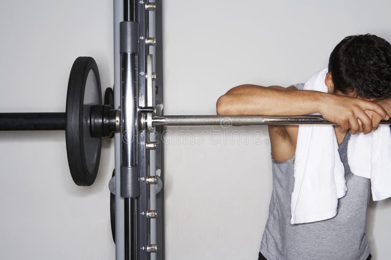 Homme fatigué se reposant sur le Barbell au gymnase image stock Homme fatigué se reposant sur le Barbell au gymnase image stock