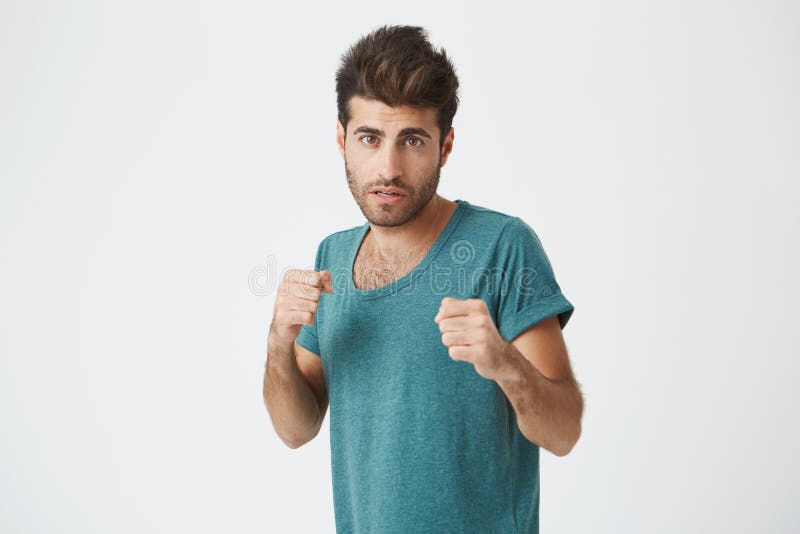 Homme fort et résolu dans le T-shirt bleu avec la barbe se tenant dans une position de combat sur un fond blanc Étudiant mâle photos stock Homme fort et résolu dans le T-shirt bleu avec la barbe se tenant dans une position de combat sur un fond blanc Étudiant mâle photos stock