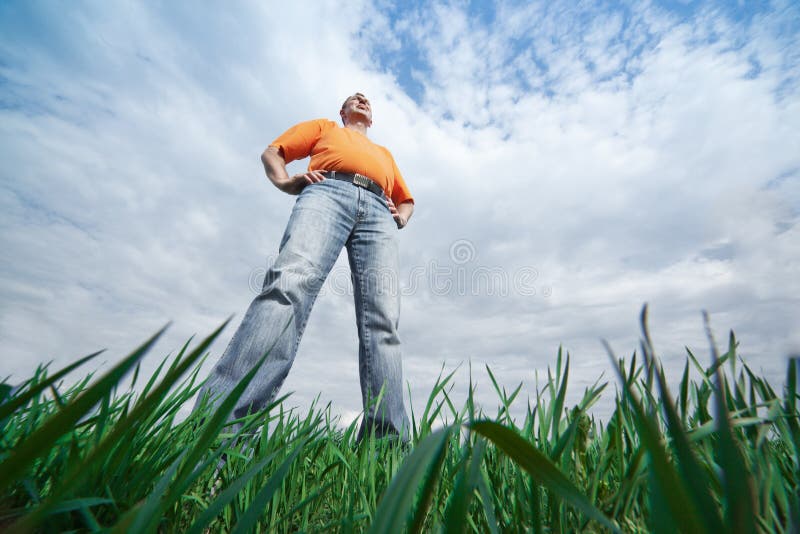 Outdoor wide-angle portrait of a tall man in jeans on blue sky and green grass background. Outdoor wide-angle portrait of a tall man in jeans on blue sky and green grass background