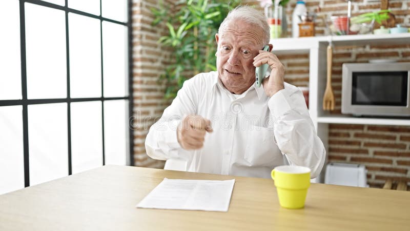 Homme grisâtre en colère se disputant sur le smartphone assis sur la table à la salle à manger