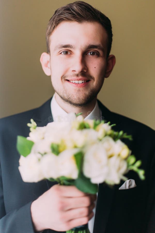 Homme habillé élégant tenant le bouquet des roses blanches d'isolement sur le fond brûlé d'or images stock Homme habillé élégant tenant le bouquet des roses blanches d'isolement sur le fond brûlé d'or images stock