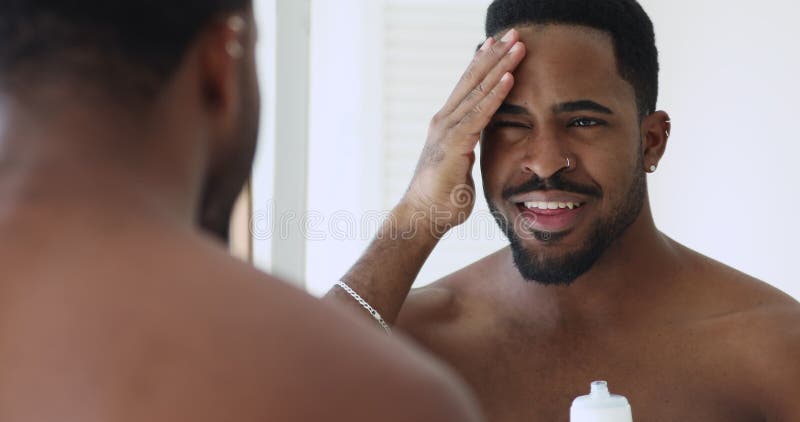 Homme heureux métisse appliquant hydratant la lotion faciale. banque de vidéos