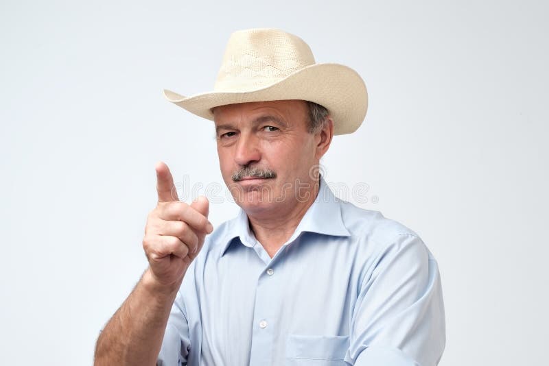 Homme hispanique mûr sérieux dans le chapeau de cowboy montrant des index, donnant le conseil ou la recommandation photographie stock Homme hispanique mûr sérieux dans le chapeau de cowboy montrant des index, donnant le conseil ou la recommandation photographie stock
