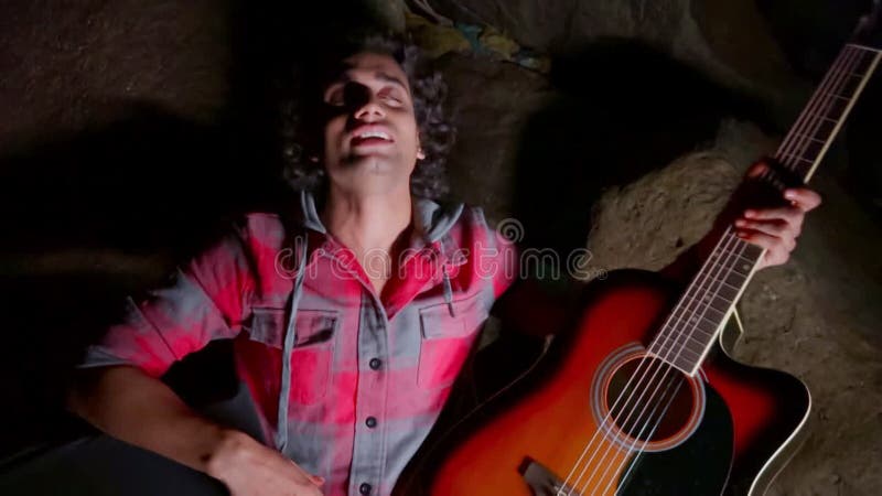 Homme ivre tenant une guitare acoustique parlant assis dans un environnement faiblement éclairé évoquant une atmosphère humoristiq clips vidéos