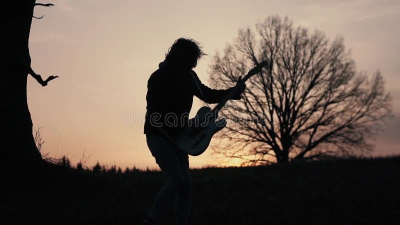 Homme jouant la guitare électrique et chantant dans un domaine près de l'arbre au coucher du soleil Silhouette