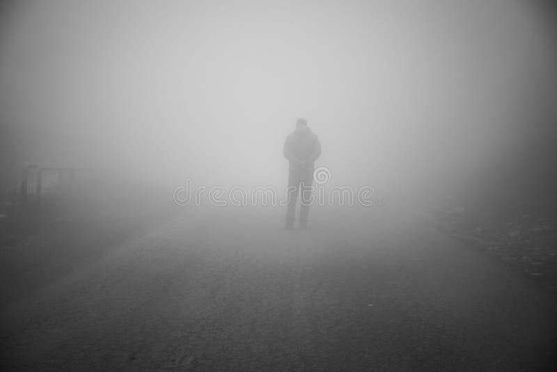 Homme marchant loin sur la route brumeuse Seul équipez debout sur la route goudronnée brumeuse et brumeuse rurale
