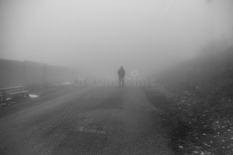 Man walking away on misty road. Man standing alone on rural foggy and misty asphalt road. Selective focus. Man walking away on misty road. Man standing alone on rural foggy and misty asphalt road. Selective focus