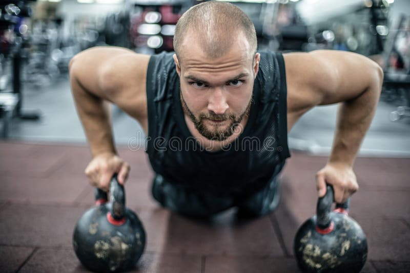 Homme musculaire bel faisant des pousées sur le kettleball dans le gymnase de crossfit photos stock Homme musculaire bel faisant des pousées sur le kettleball dans le gymnase de crossfit photos stock