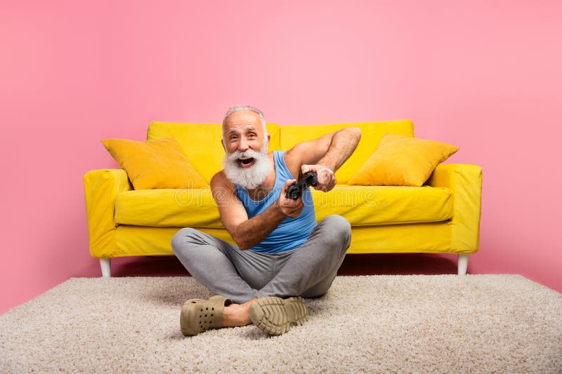 Homme mûr joyeux jouant à des jeux vidéo à l'intérieur sur fond rose et assis sur une moquette au sol photos libres de droits