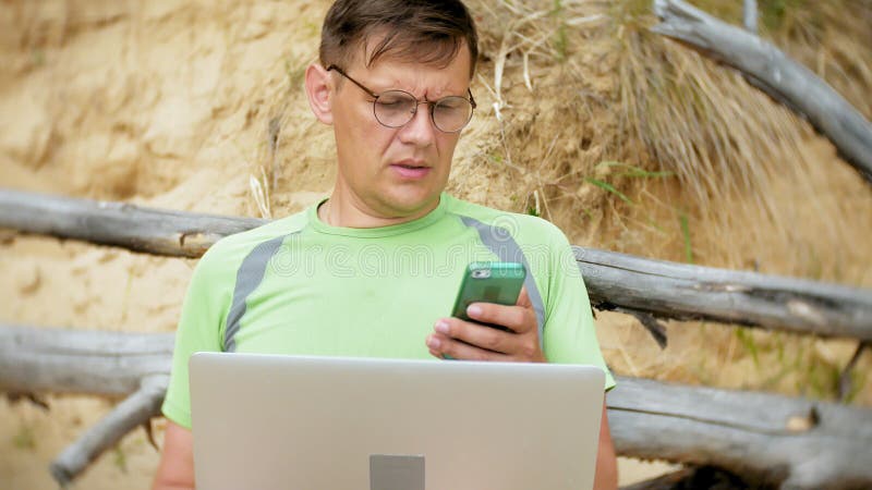 Homme mûr occupé travaillant sur un ordinateur portable avec des papiers d'affaires prenant un téléphone pour travailler un appel