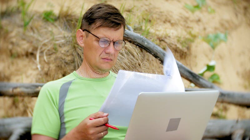 Homme mûr occupé travaillant sur un ordinateur portable avec des papiers d'affaires prenant un téléphone pour travailler un appel